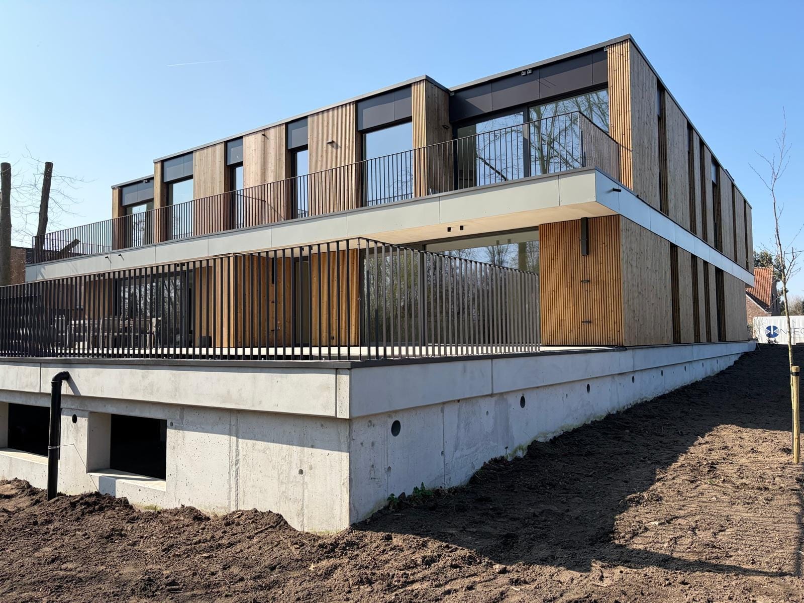 Afgewerkt appartementsgebouw met houten gevelbekleding en platte daken onder een blauwe hemel.