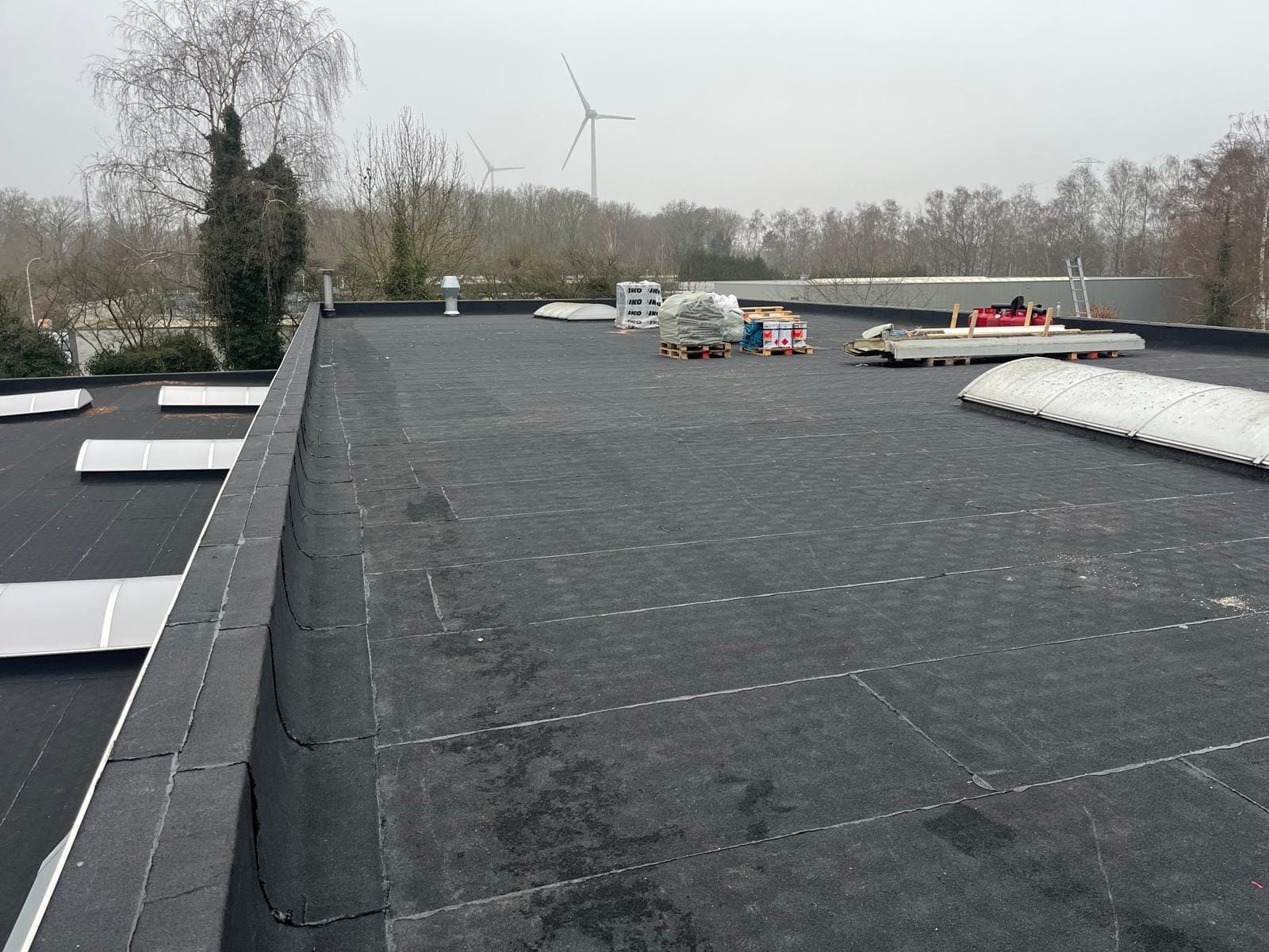 Uitgestrekt industrieel plat dak met lichtstraten en windturbines aan de horizon.