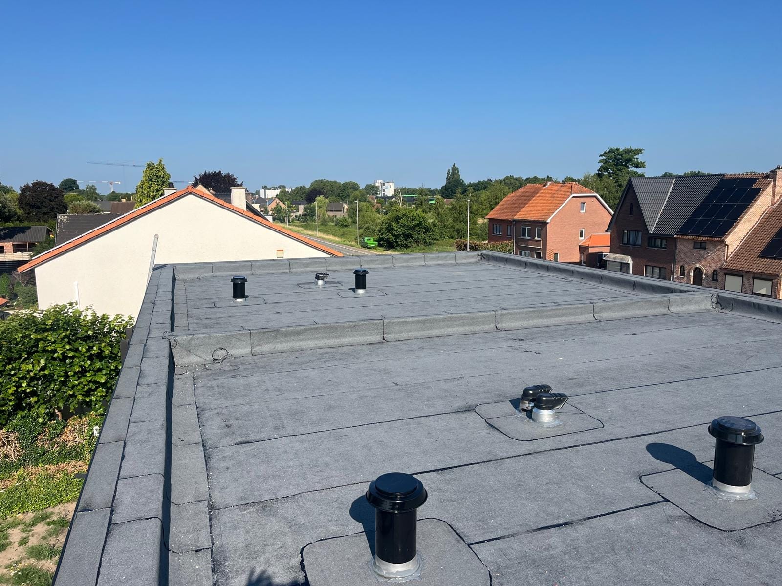 Groot grijs plat dak met ontluchtingskappen onder een diepblauwe lucht.