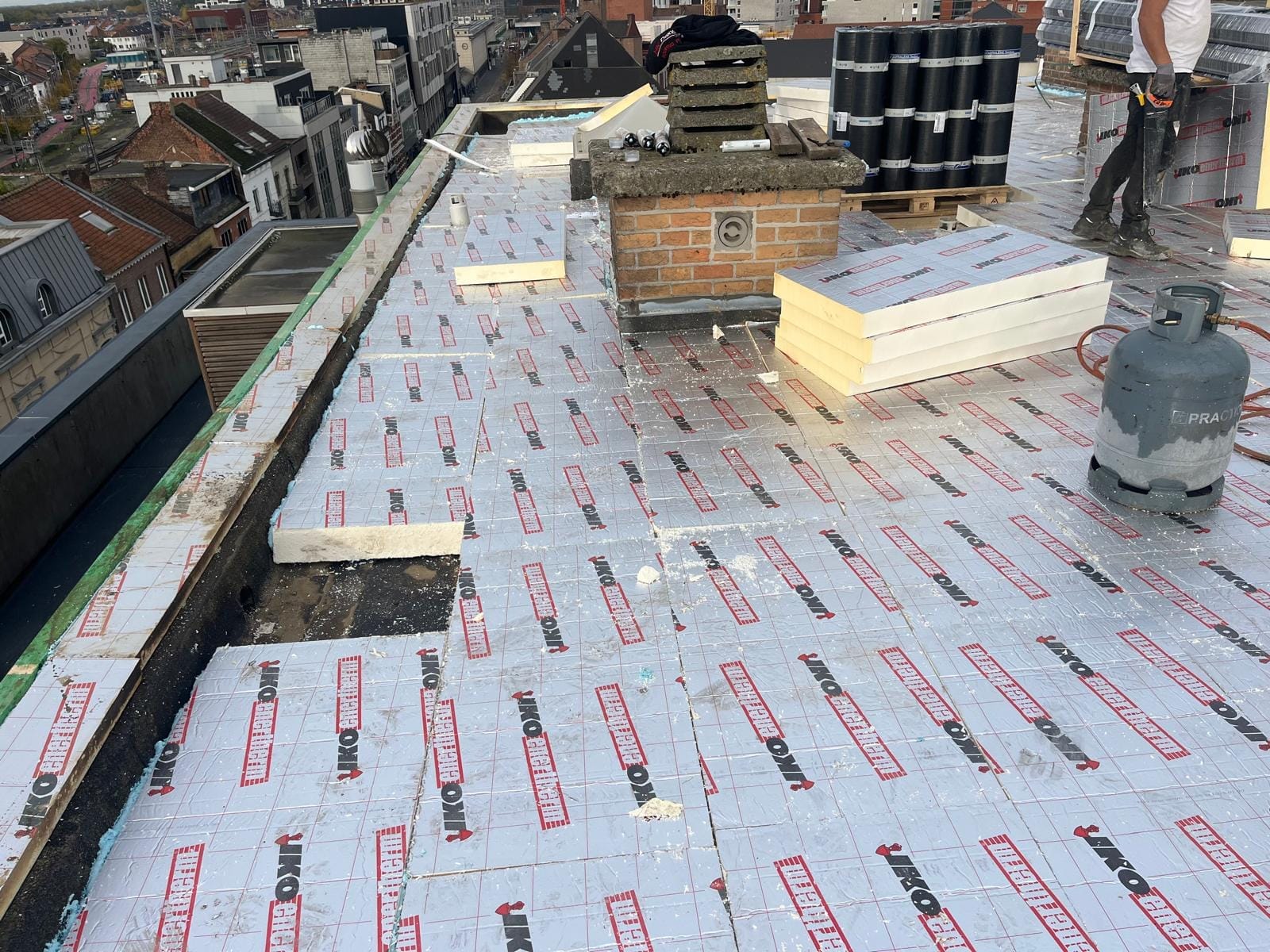 Stadsdak in uitvoering met nieuw geplaatste isolatieplaten en uitzicht over de winkelstraat.