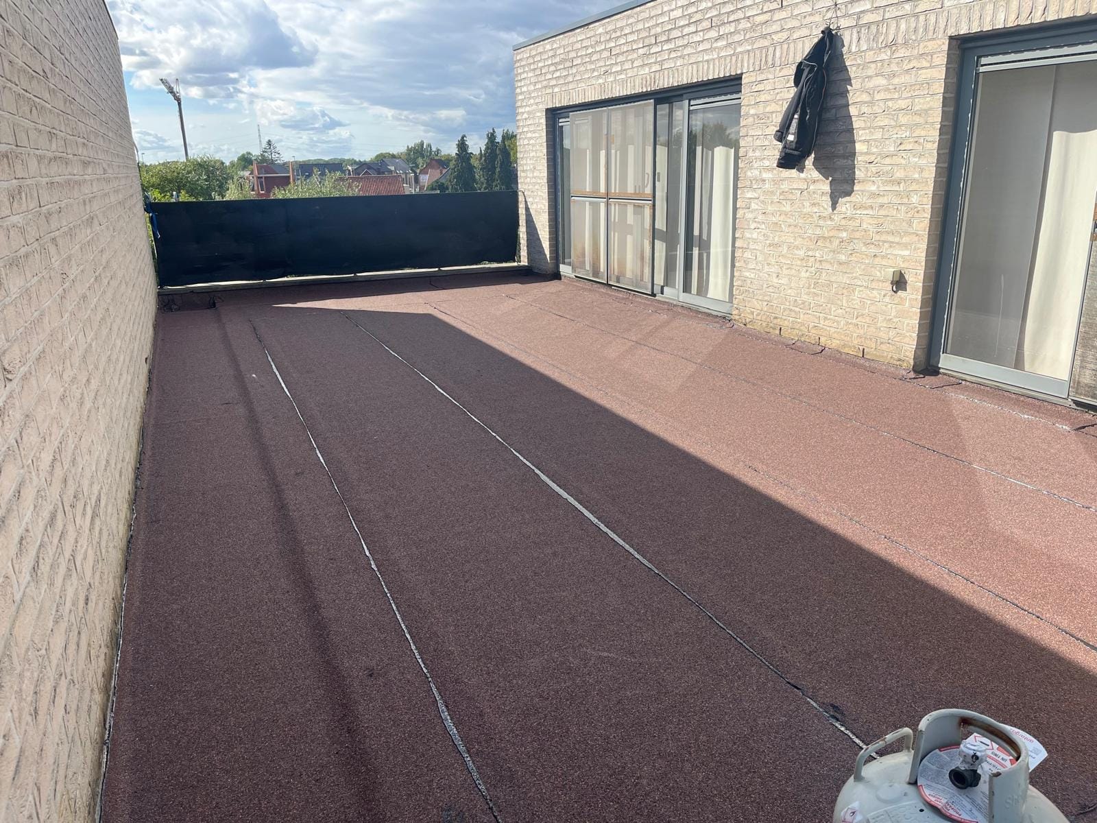 Afgewerkt dakterras met roodgekleurde minerale bedekking tussen bakstenen muren.